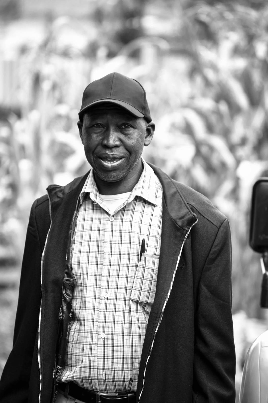 Andrew Kongo Ogechi in a black cap, jacket and checked shirt, smiling gently at the camera