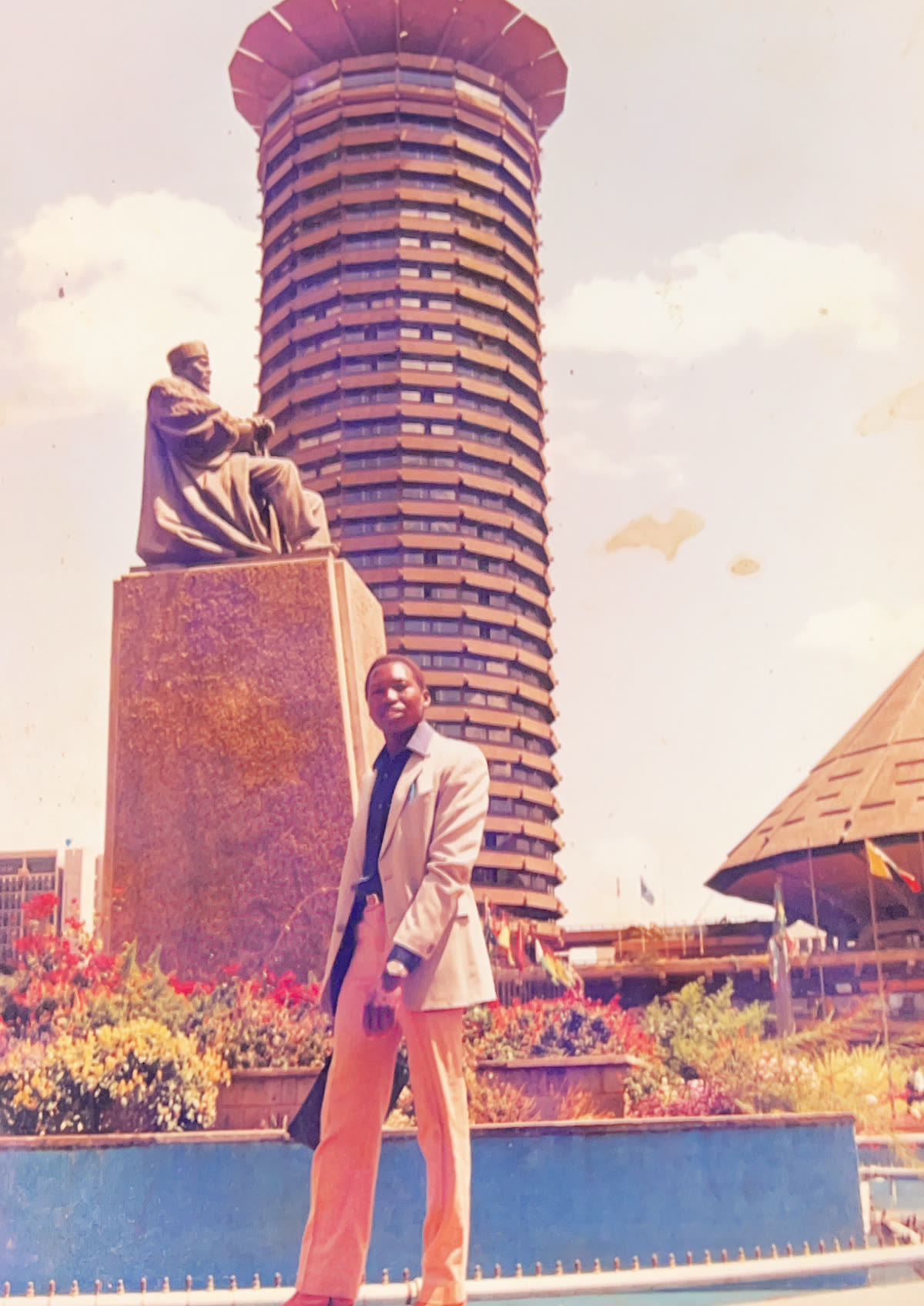 Andrew standing beside the Jomo Kenyatta statue, with the KICC tower behind him.