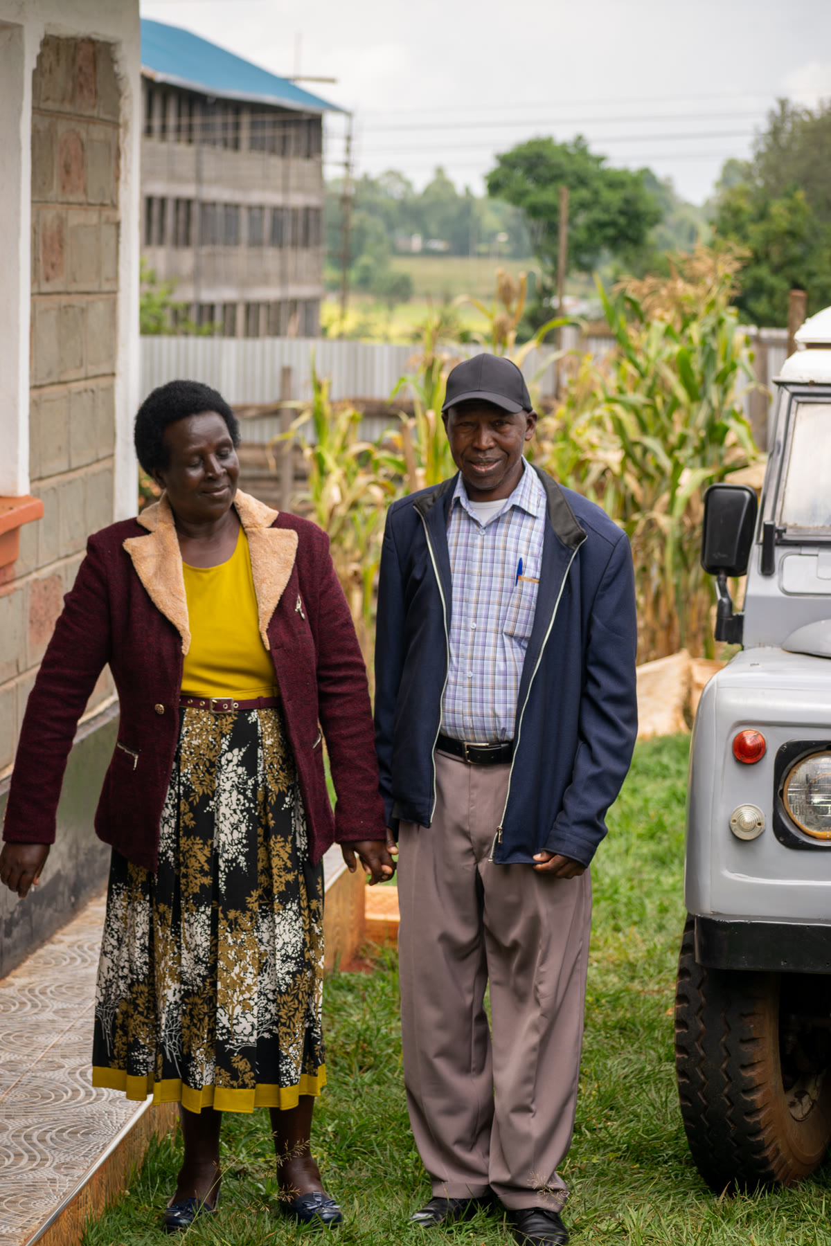 Andrew standing beside a woman outside a house, with a vehicle parked nearby.
