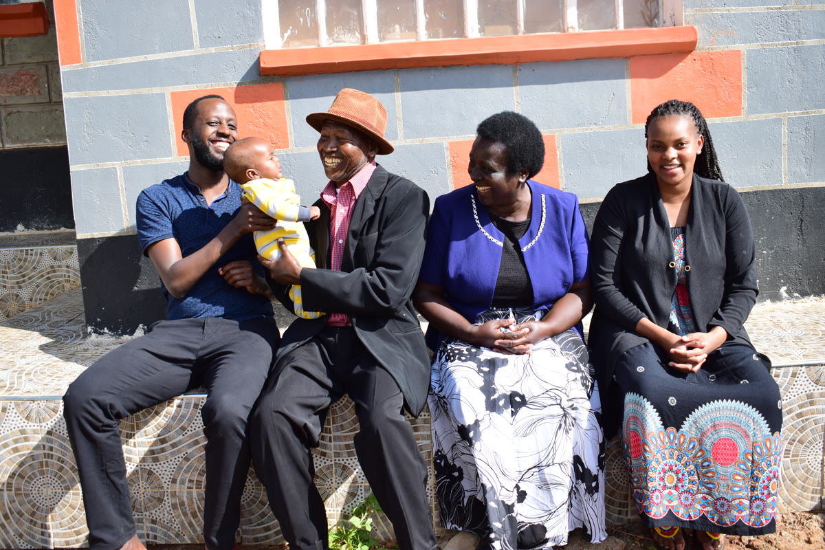 Four adults and a baby smiling together on outdoor steps.